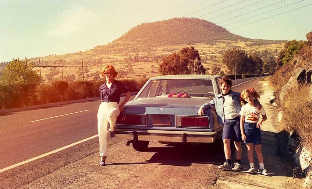 Family posing by car on scenic road.