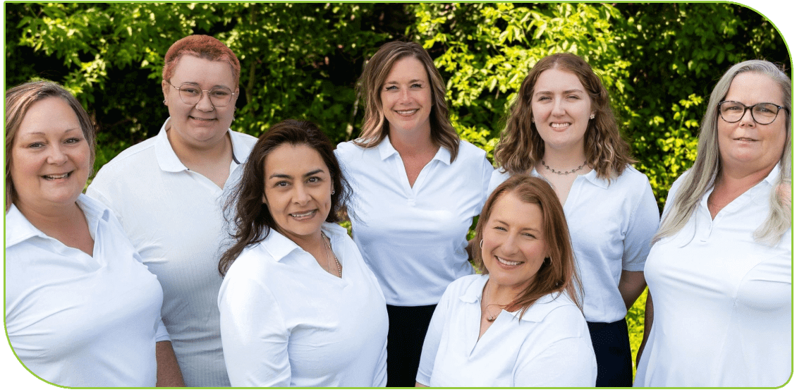 Seven women in white shirts smiling outside.