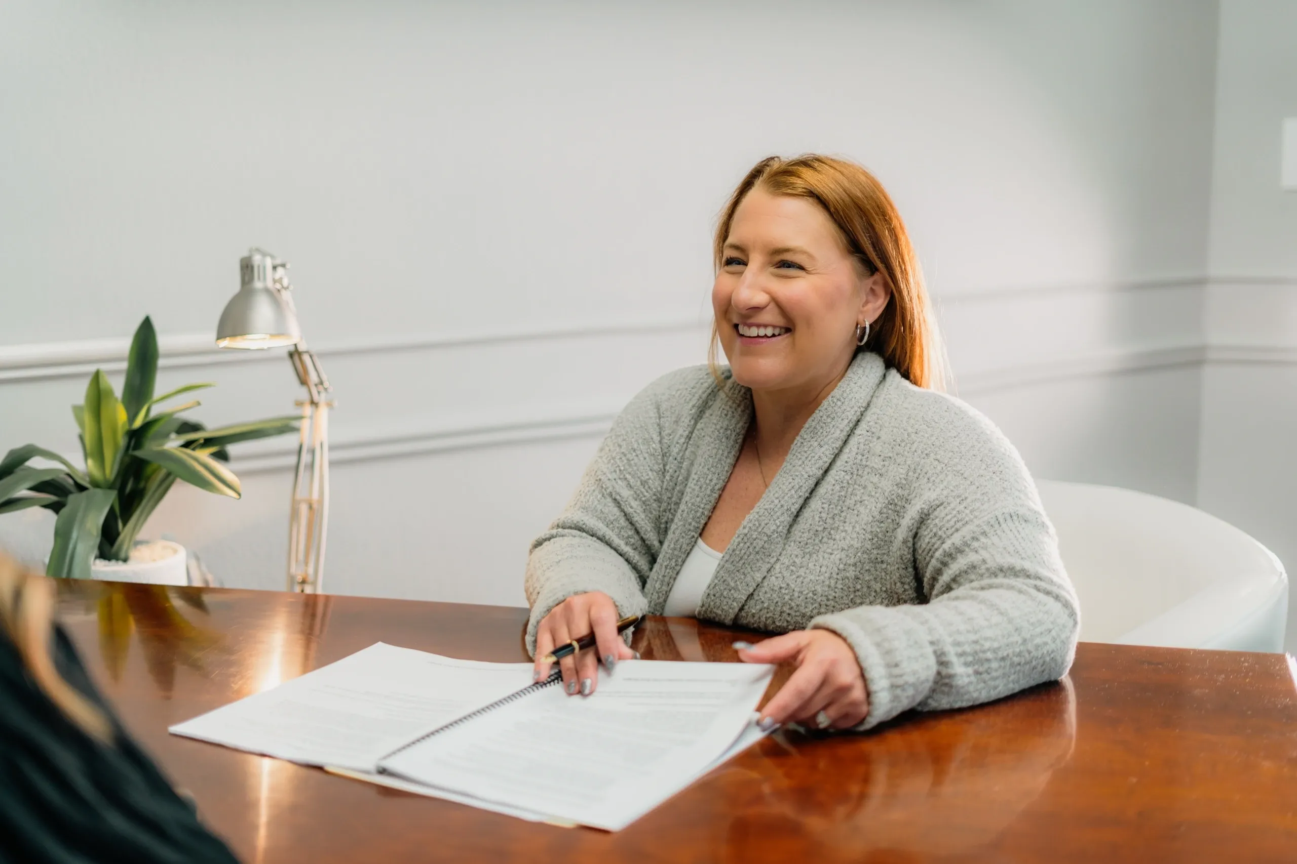 Smiling woman holding papers at desk.