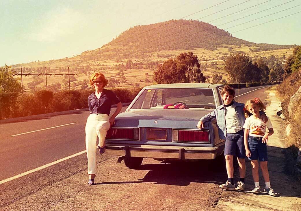 Family posing by car on scenic road.