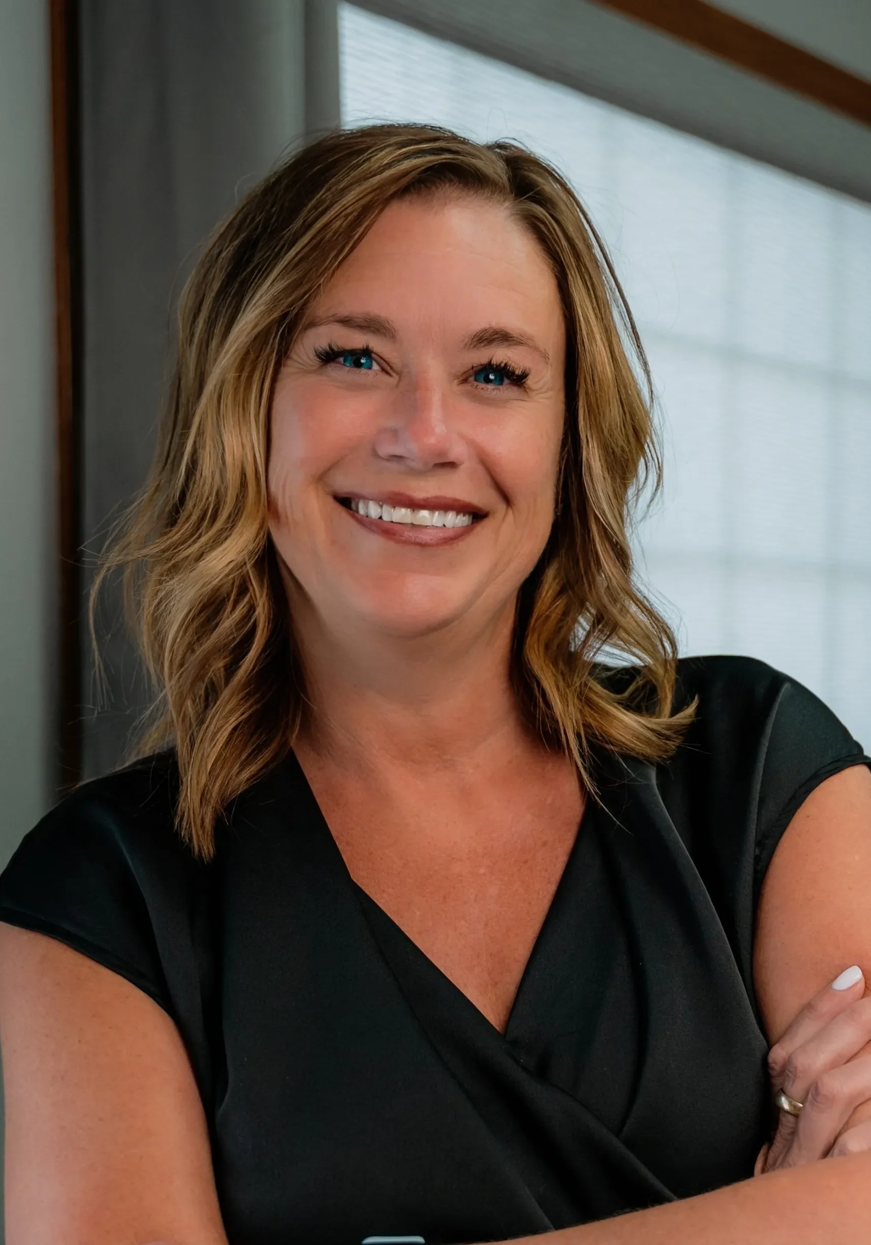 Smiling woman in black dress, arms crossed.
